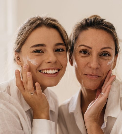 close-up-two-cute-caucasian-women-smearing-their-face-with-cream-looking-camera-white-background-beauty-youth-concept